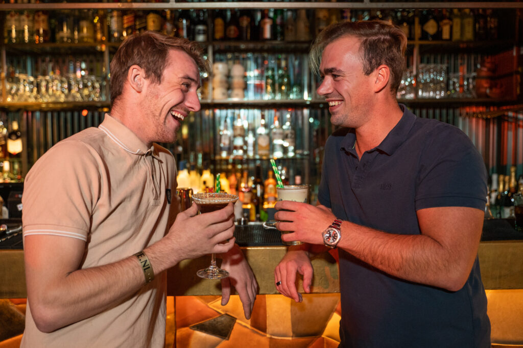 Twee lachende jongens die hun glas omhoog houden tijdens een cocktail workshop