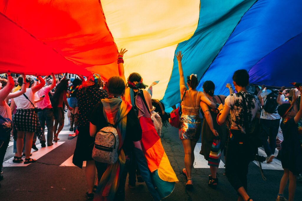 People walking under a coloured flag during a gay pride. 